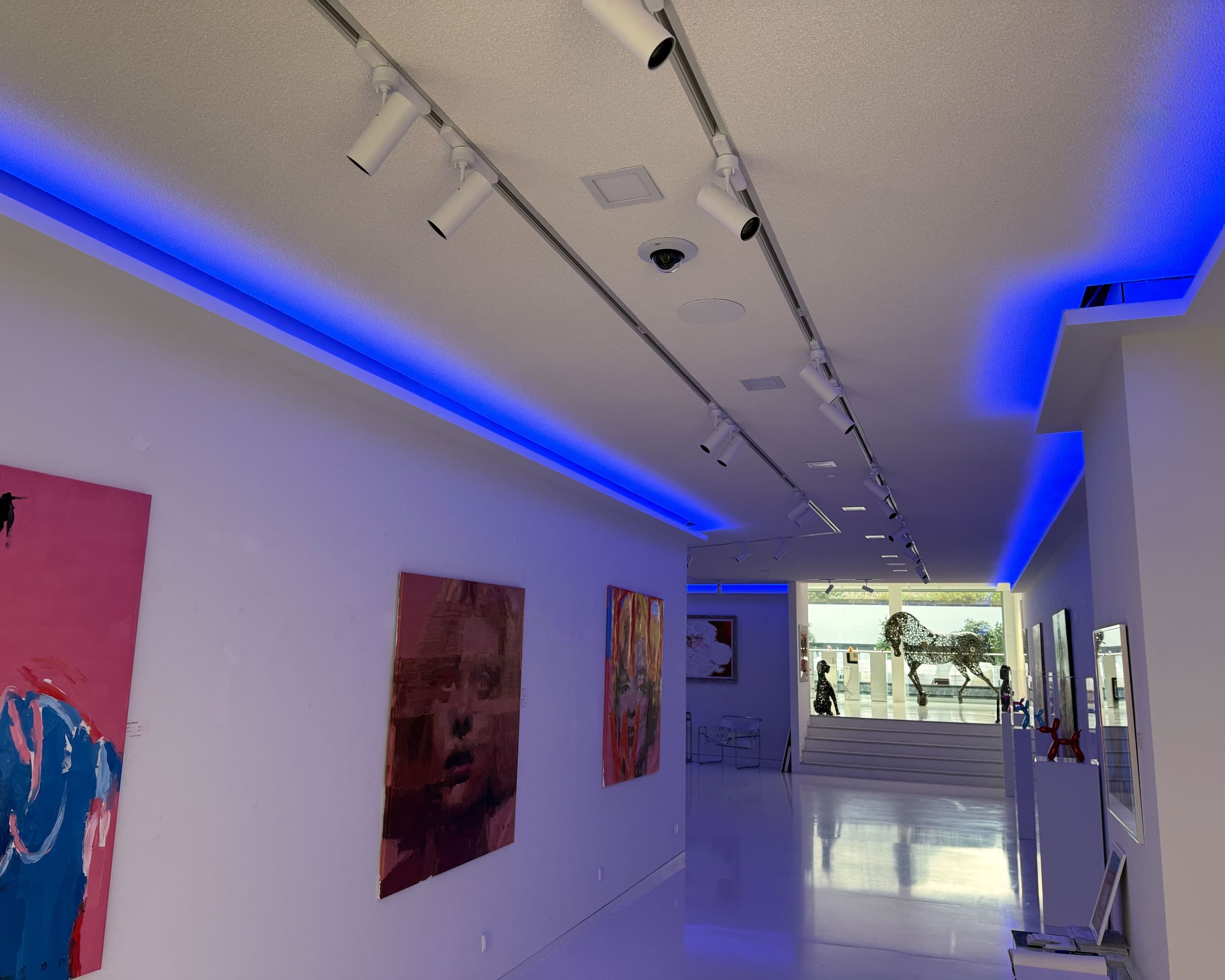 Moderne Kunstgalerie mit blauem LED-Lichtband und dezent in die Decke integrierter Dome-Kamera.
