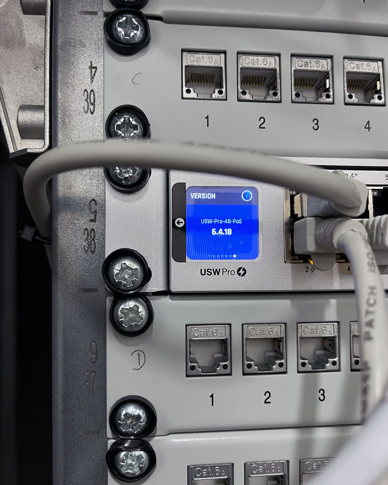 UniFi USW-Pro-48-PoE Switch mit Display zwischen Cat.6A-Patchfeldern in einem sauber verdrahteten Netzwerkschrank.